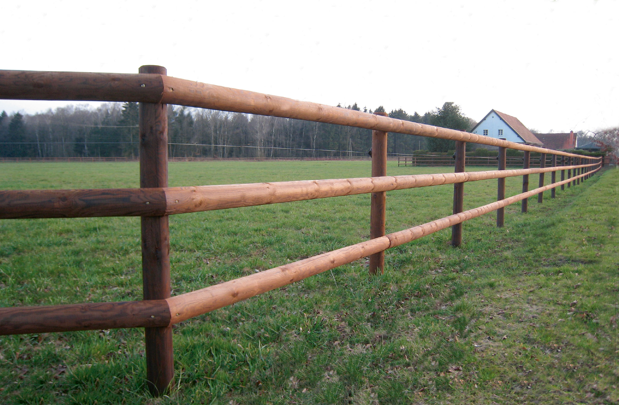 En tom hästhage med ett staket med tre lattor i förgrunden.