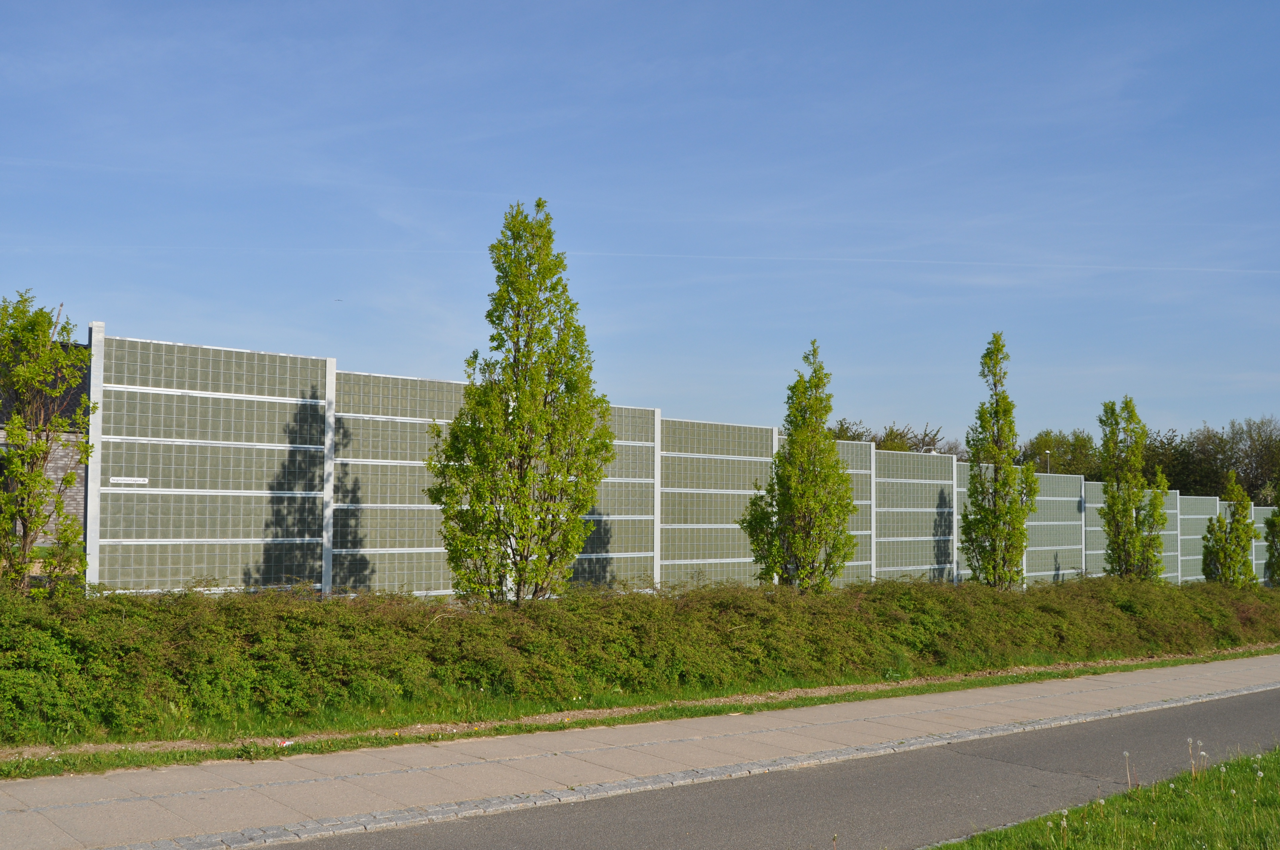 Ett Noistop® Steel bullerplank från Poda Stängsel omgivet av buskar och träd.