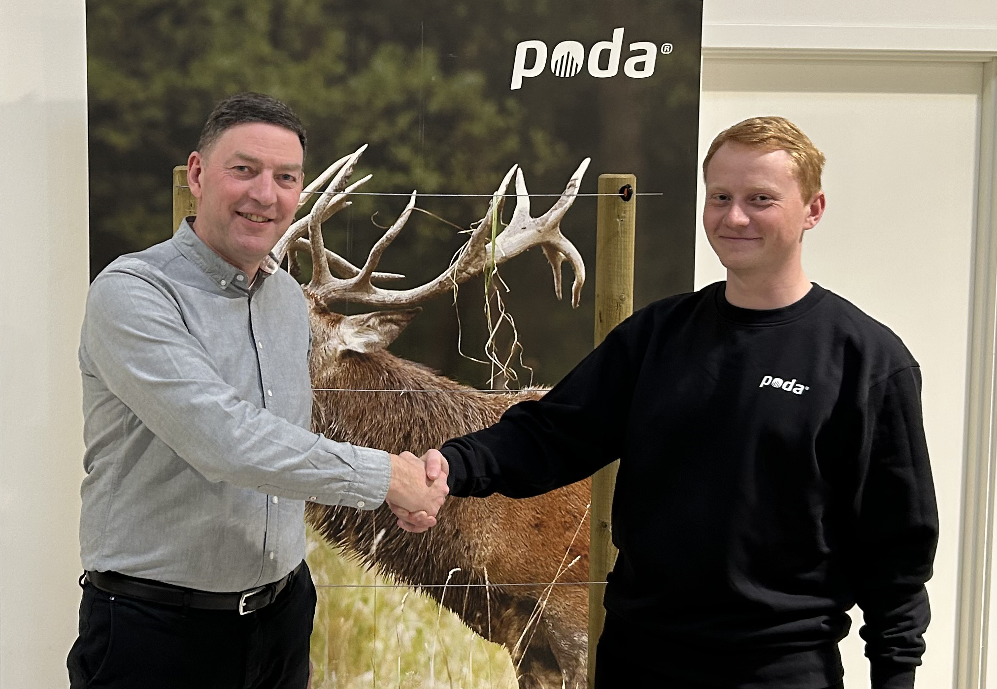 Podas direktör Peter skakar hand med Sofus från det nya Poda-centret, Poda Hegn Ringe, framför en banderoll med kronhjort och elstängsel.