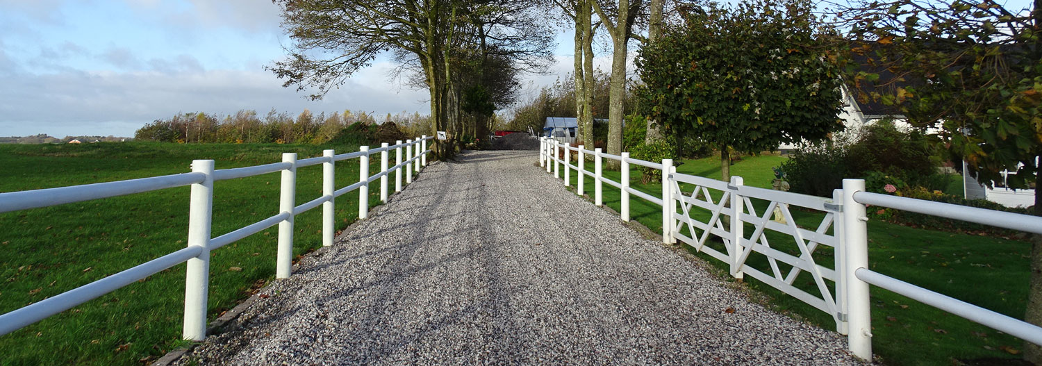 En uppfart med ett vitt staket på båda sidor leder upp till en lantgård.