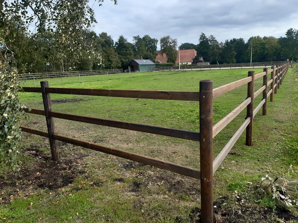 I förgrunden finns en tom hästhage med ett Colorado häststängsel. I bakgrunden syns en villa.