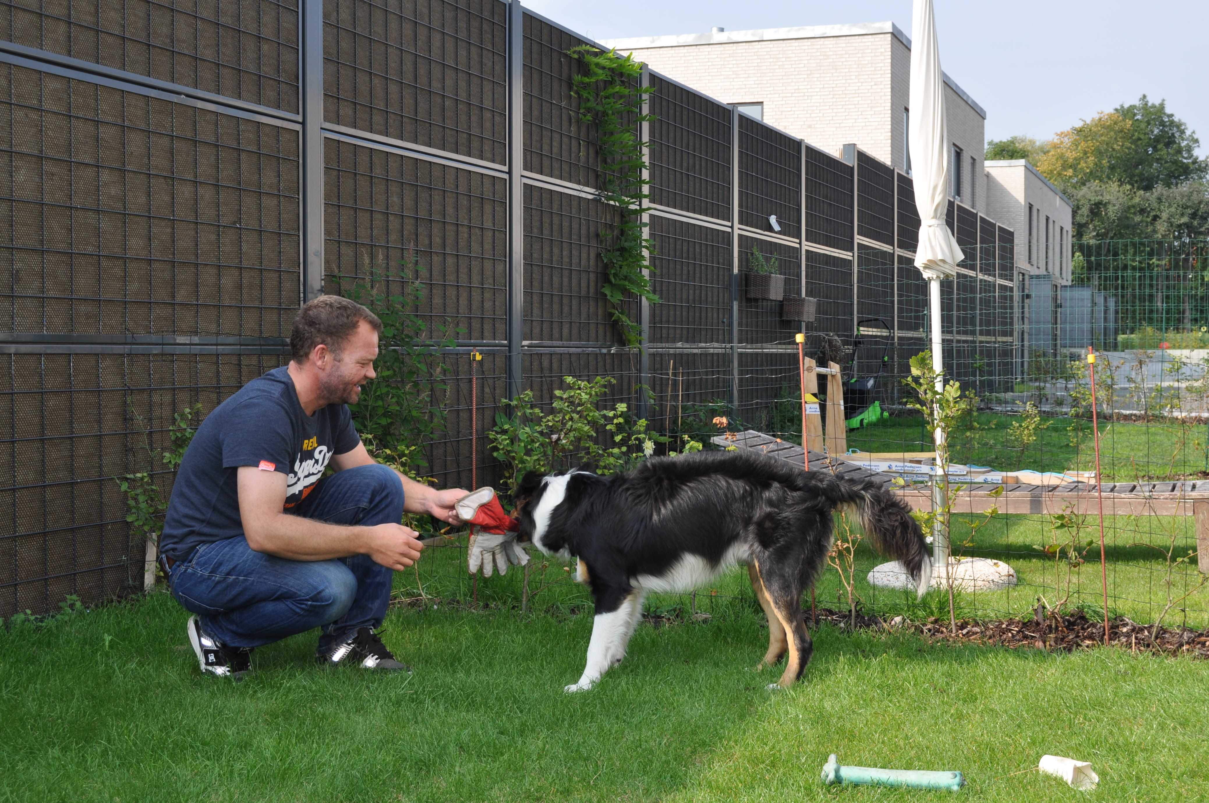 En man och hans hund sitter framför ett Noistop® Steel bullerplank från Poda Stängsel. Monterat i en trädgård som avskärmning till grannarna.