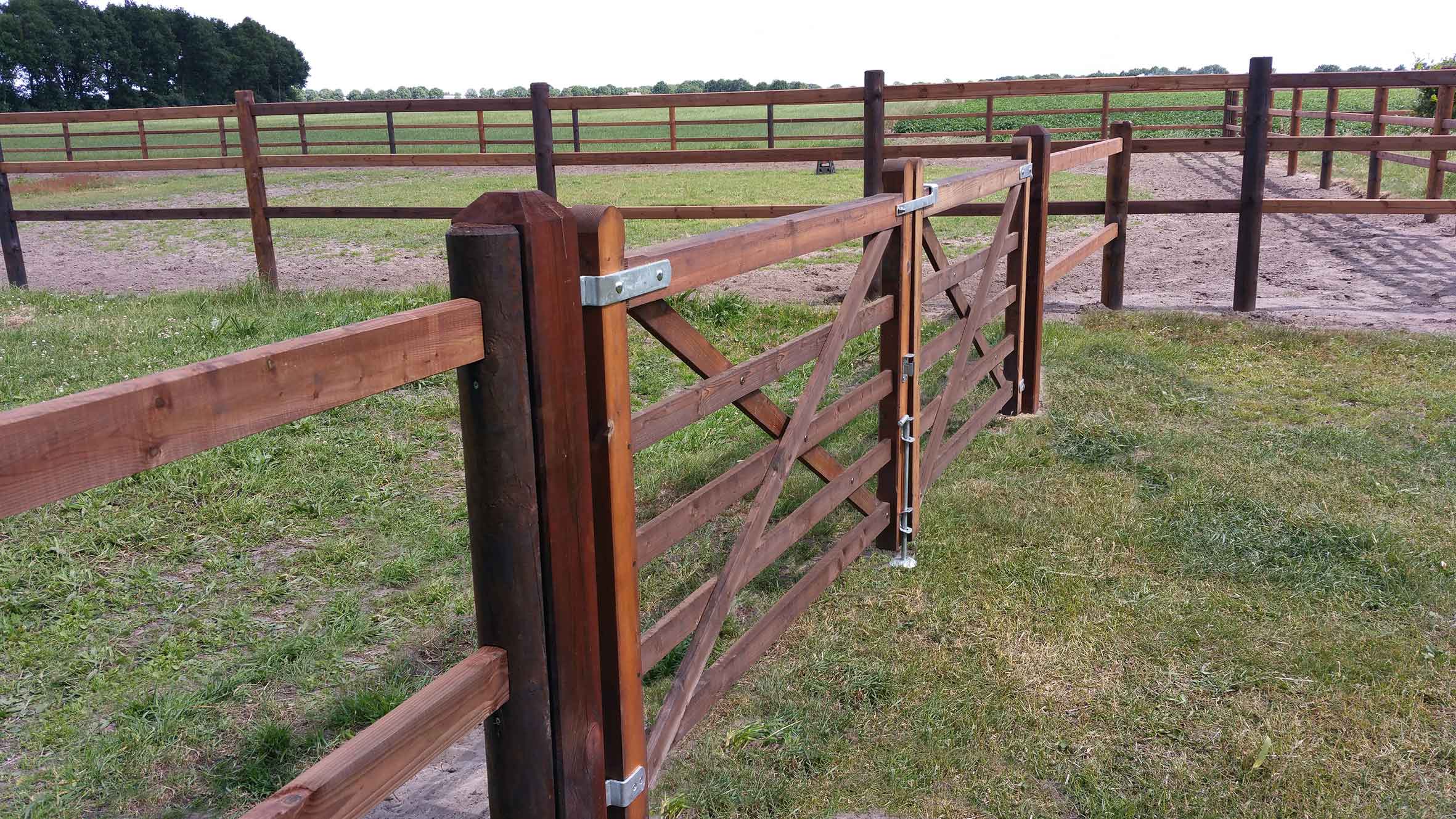Ett häststängsel skiljer två hästhagar från varandra. En dubbel trägrind ger tillgång till den ena hästhagen.