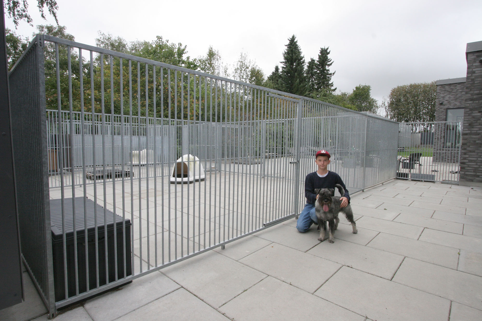 En pojke knäböjer framför en hundgård med sin hund.