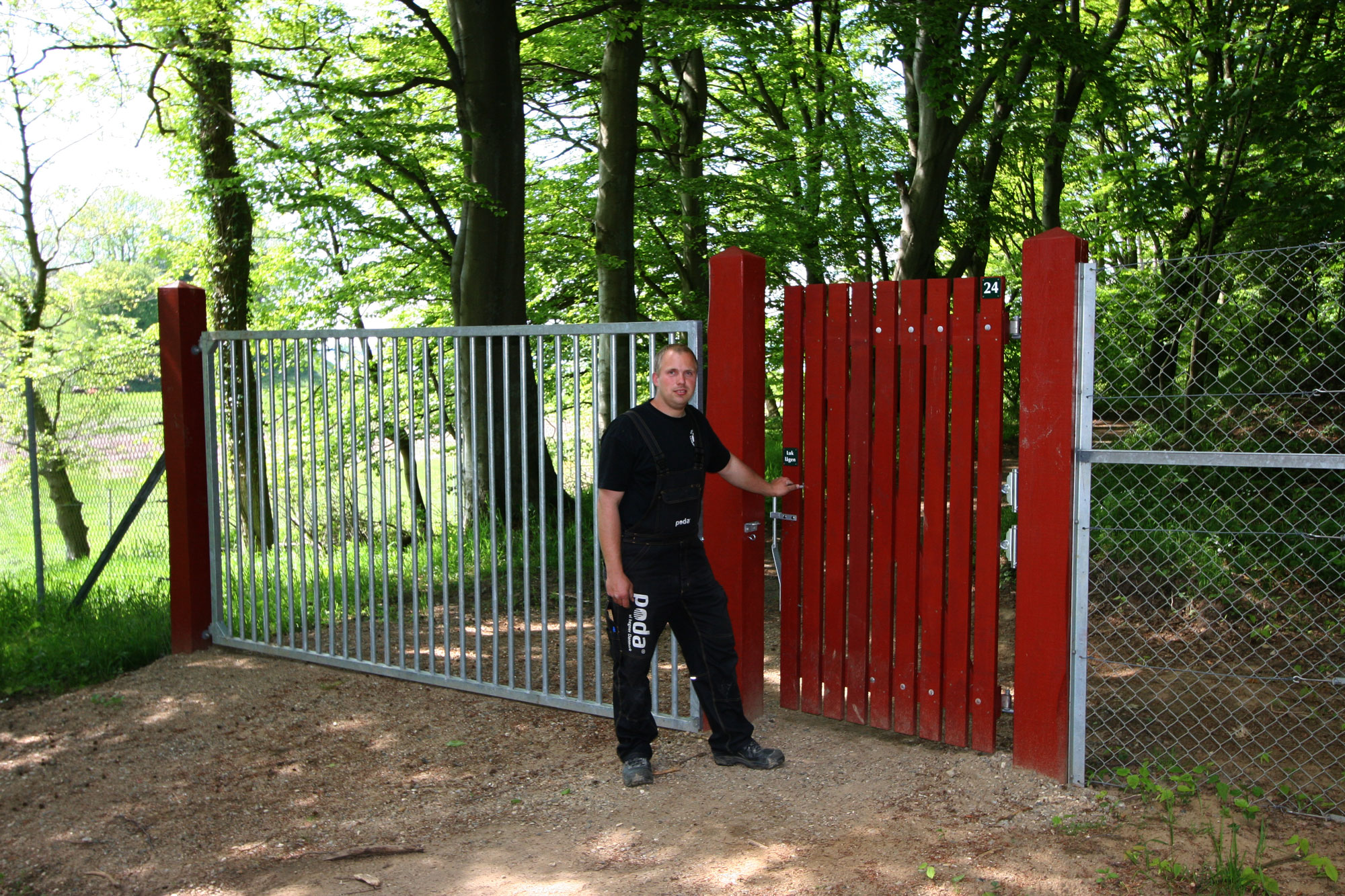 En man står framför en röd trägrind som leder in till en djurpark. Bredvid grinden finns en port av stål.