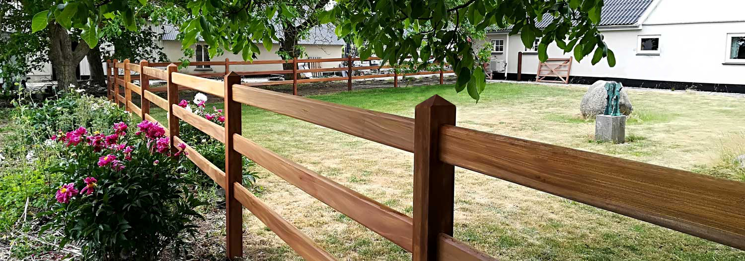 Ett Oxford staket av hårdträ gränsar till ett lantställe i en trädgård på landet